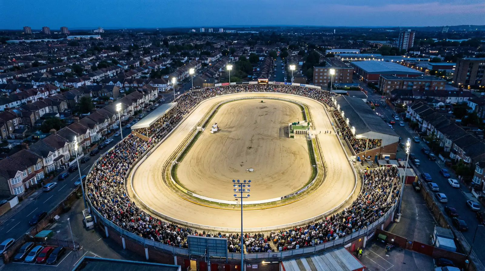 Aerial view of a floodlit greyhound racing stadium with sand oval track